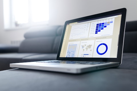 An open laptop displaying analytics dashboards with charts, graphs, and data visualizations on the screen, placed on a grey sofa.